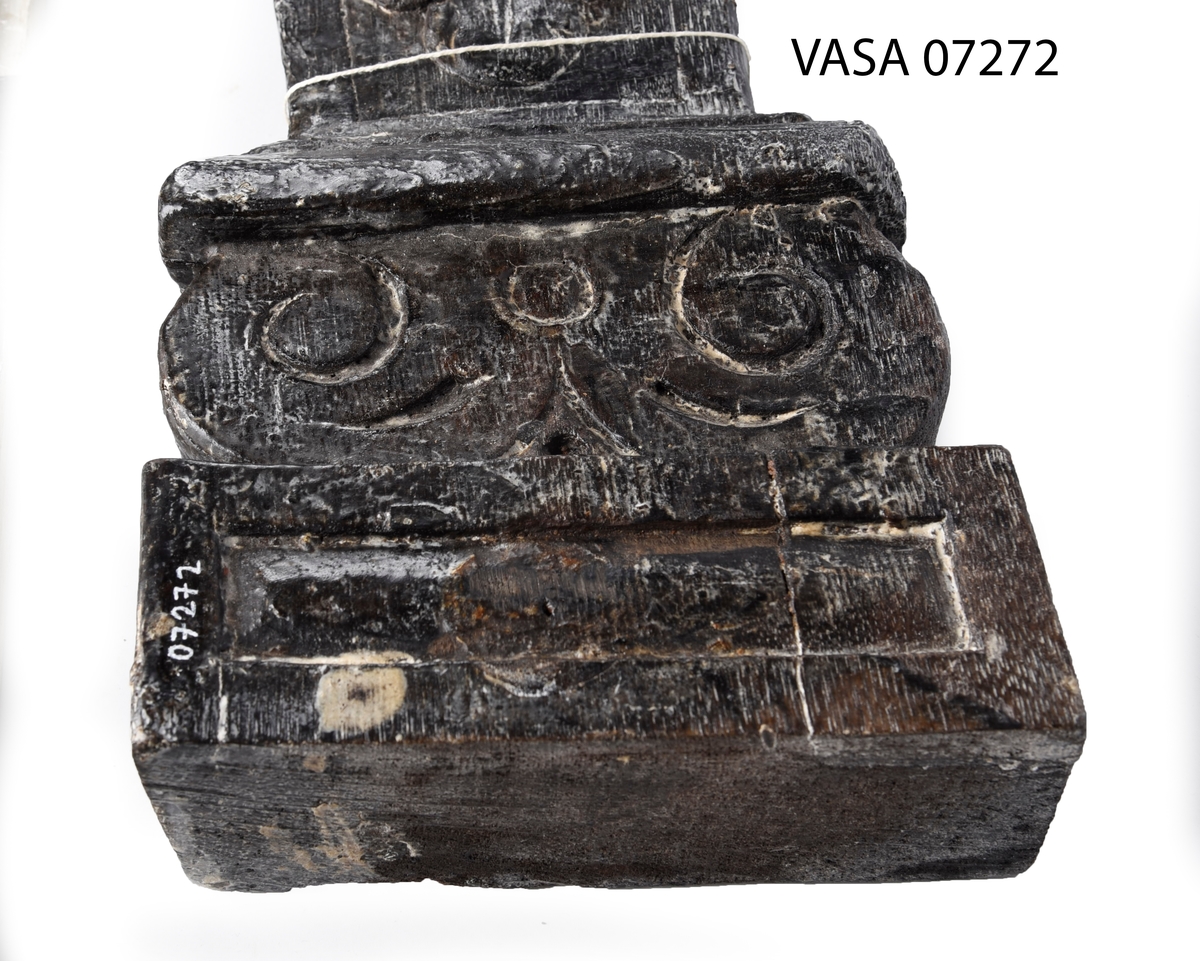 Liten skulpterad pilaster, utformad som en karyatid eller möjligen en putto. Figuren har långt hår och ett knubbigt ansikte, omgivet av en bred krage. Det nedåt avsmalnande pilasterskaftet är dekorerat med akantusblad. Nedtill avslutas pilastern av en rikt profilerad och dekorerad sockel. På skulpturens släta baksida sitter en nygjord upphängningsanordning, fästad med två skruvar.
Skulpturen är sliten.

Text in English: A small carved pilaster, with a caryatid or probably a putto. The figure has a chubby face, long hair and a broad collar. The lower part of the pilaster is decorated with acanthus leaves. The caryatid stands on a richly profiled and decorated socle. On the smooth back of the sculpture is a new hanging device attached with two screws.
The sculpture is worn.