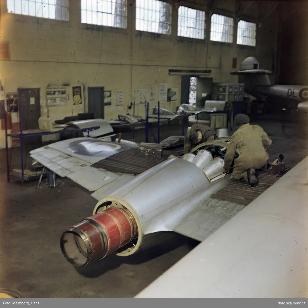 Brittiska flygvapnet, Royal Air Force (RAF). Två mekaniker arbetar med en jetmotor (Rolls Royce Derwent) på ett jaktplan av typen Gloster Meteor F.4. i en hangar. Troligen flygbasen Duxford i Cambridgeshire, England.