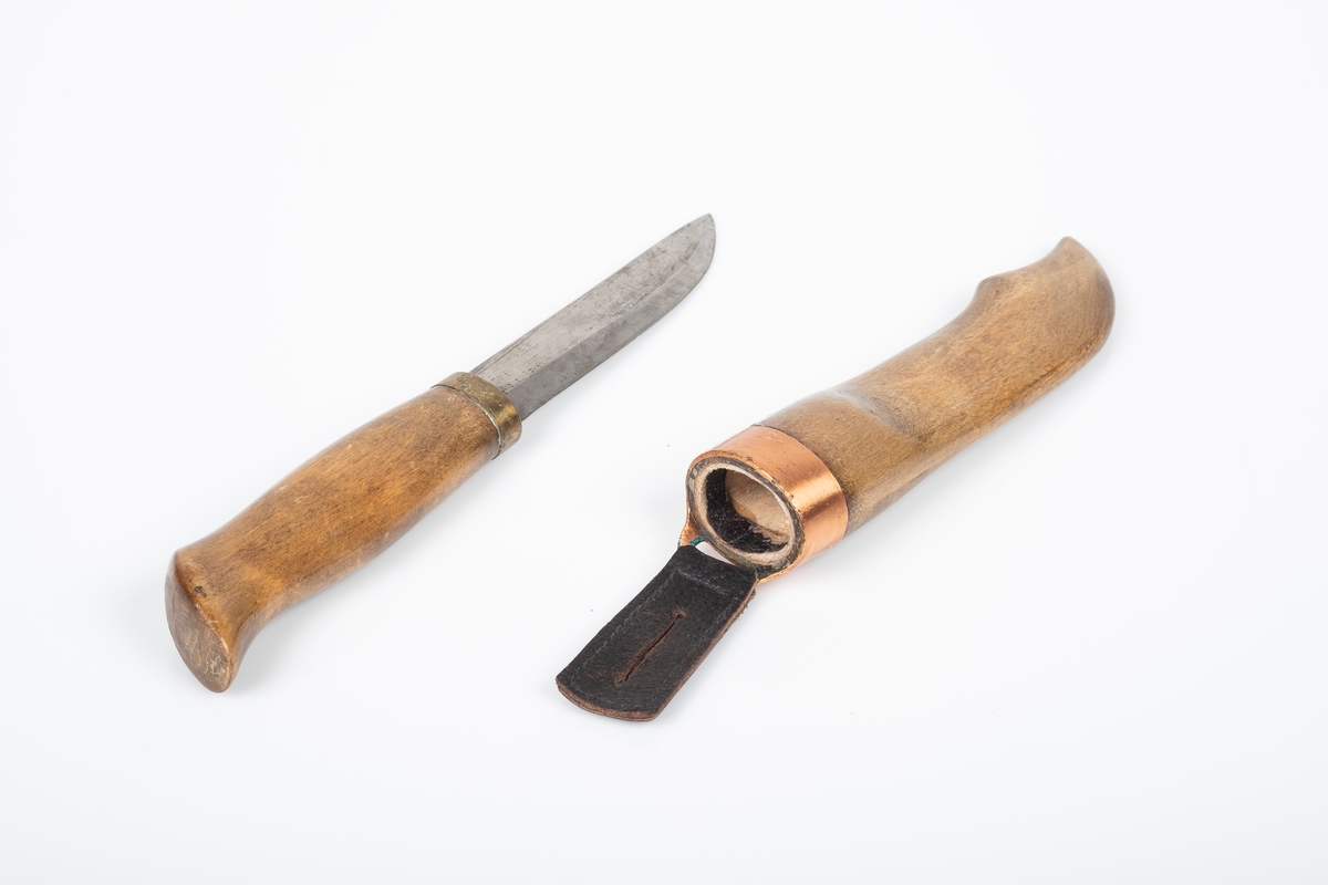 Håndlaget tollekniv med skaft og slire av tre, og knivblad av metall. Skaften og sliren er lakkert med blank lakk. Sliren er pyntet med kobberkant. Fra kobberkanten henger en svart skinnlapp med hull i til oppheng. Bolsteret er av messing.