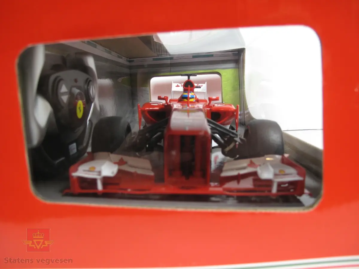 Miniatyr, lekebil i eske. Laget av papp og plast med hovedfargen rød, men den har noen fargerike striper, under plast vinduet. Bilen er rød og har litt reklame på seg, tallet 3 er på panseret, den er og radiostyrt. Skala. 1:12