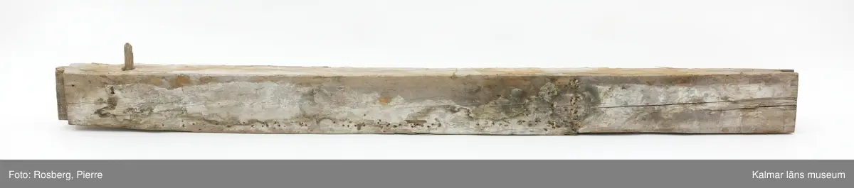 KLM 17275:4:2. Vägg, del av. En timmerstock tillhörande en innervägg. En trädymling sitter i stocken. På båda sidor bevarade fragment av bemålning, troligen från 1600-talet. På båda sidor måleri i grått, grönt och vitt med rombiska eller runda figurer i svart och rött. På ena sidan även rester av påspikade tapeter.