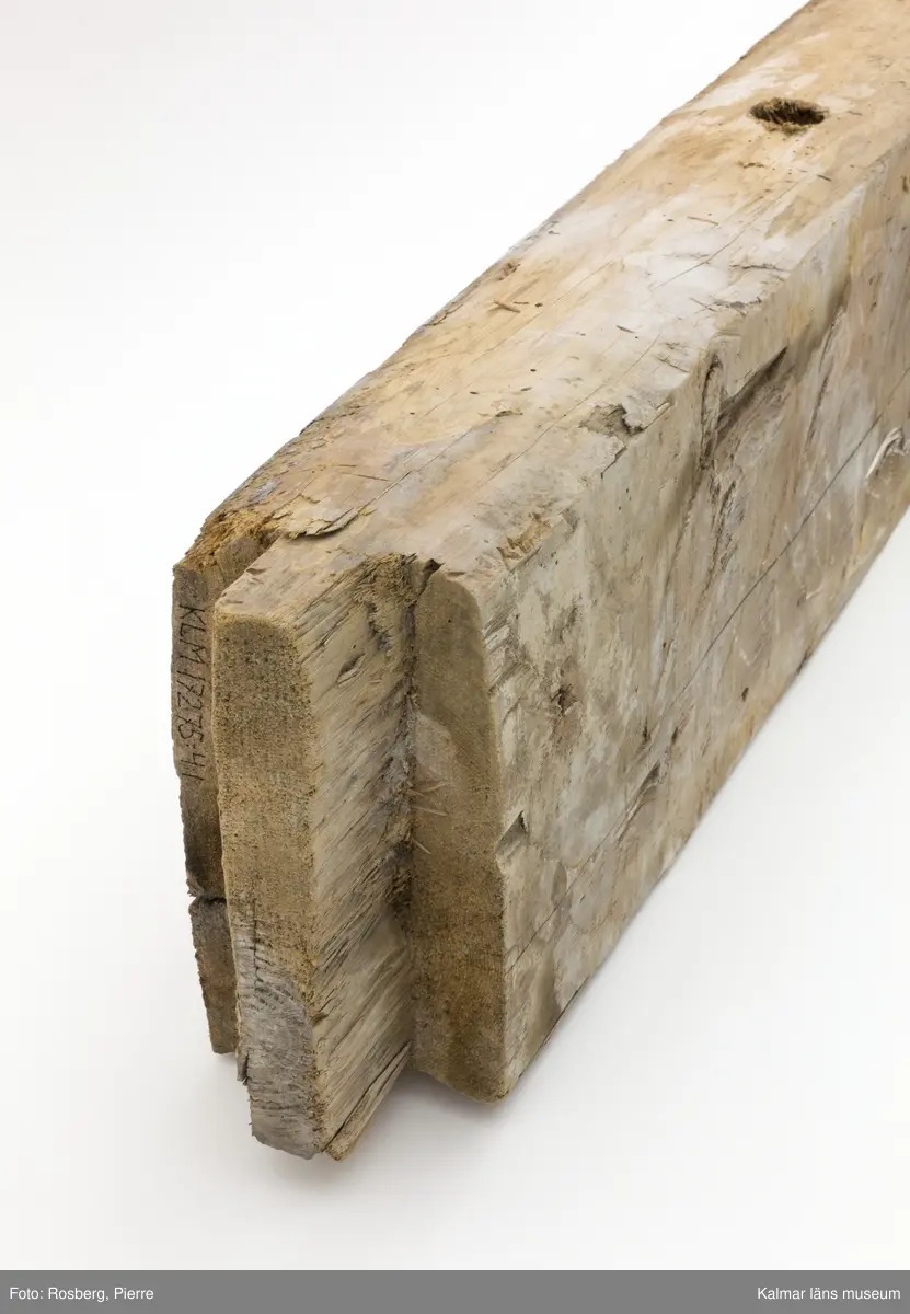 KLM 17275:4:1. Vägg, del av. En timmerstock tillhörande en innervägg. Hål för trädymlingar. På båda sidor bevarade fragment av bemålning, troligen från 1600-talet. På ena sidan måleri i bl.a. vitt och blått. På andra sidan bemålning i vitt, blått och grönt samt rester av påspikade tapeter. Även text skrivet med blyerts, något otydlig men troligen: Lundgren.
