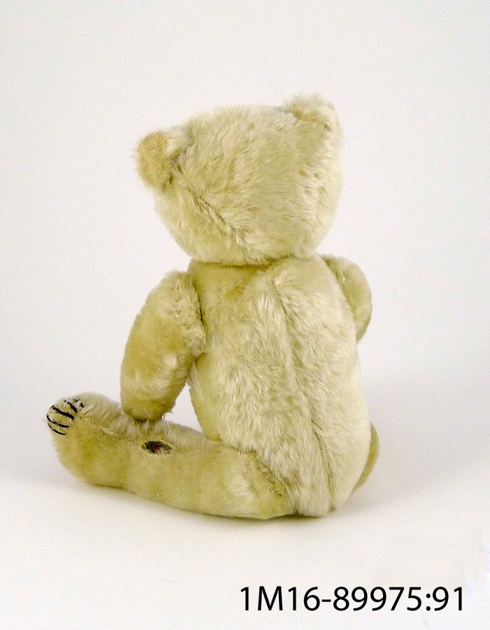 Teddybjörn av vit plysch med trampdynor av brun filt, klor av svart tråd, bruna ögon av glas samt mun och näsa i svart, defekt.