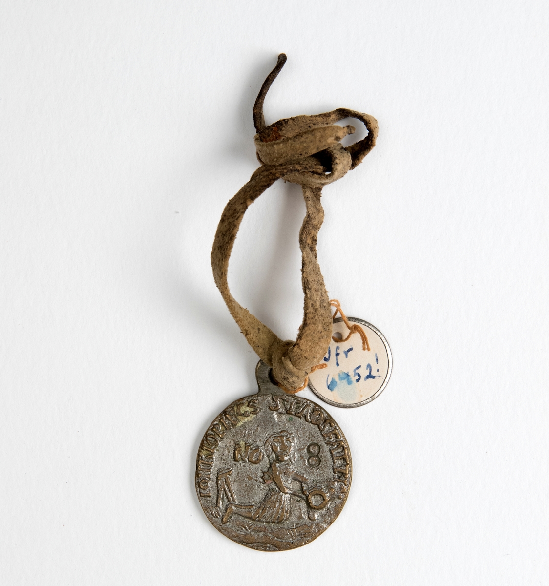 Gjutet runt märke av vit metall med text i relief på båda sidorna: "Jonkiopings stads [...] No 8", samt ett motiv av en sjöjungfru. Enligt accessionskatalogen 1904 står det felaktigt "No 11". Ett ljust läderband är knutet i märket. En liten rund pappbricka är vidhängd märket, märkt; "Jfr 6452!"