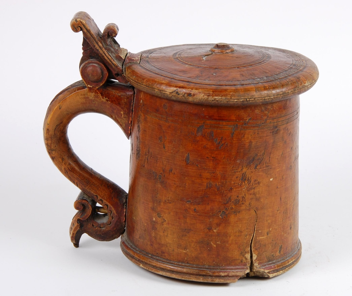 Kanne av dreid valbjørk. Lokket med dreide ringer. Bladformet lokkåpner. Hank med utskjæringer, ender i en spiss med bladdekor. Korpus med dreide ringformete bårder øverst,  fire målemerker innvendig.