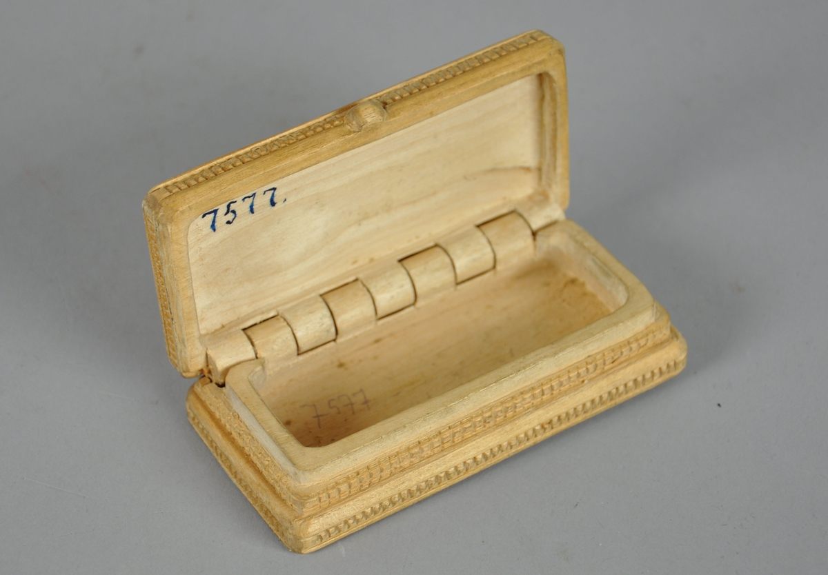 Liten eske av tre, med skjært dekor. Esken har en rektangulær utforming og skjært dekor på lokk og bunn med akantusmotiv, og linjer/rutenett på sidene. 

Esken har en knott på framsiden av lokket.