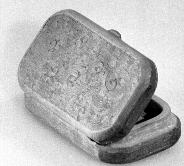 Rektangulær eske av tre, med avrundede kanter. På lokk og underside er det innrisset sirkulære streker. 

Dypere hakk enkelte steder i innrissingen kan tyde på at den dekorative treskjæringen er uferdig.