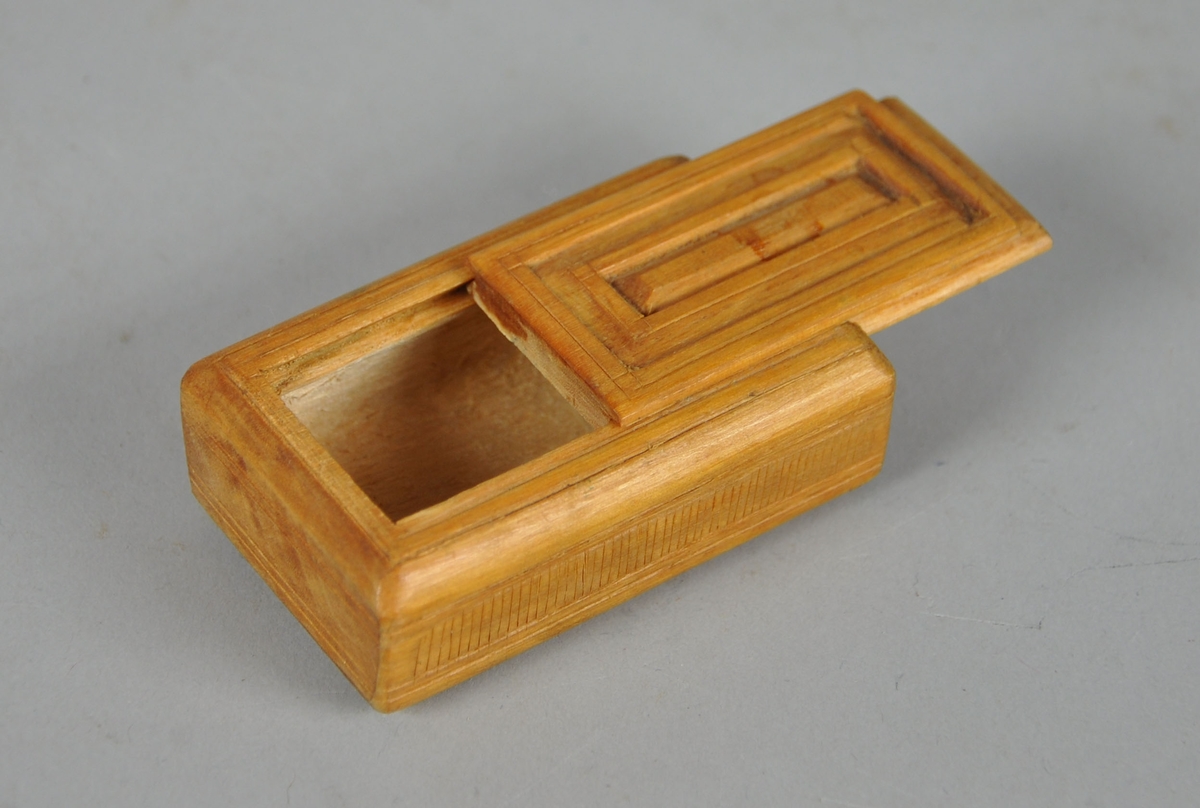 Eske av tre, med skyvelokk. Lokk og underside av eske er dekorativ utformet med treskjæring.