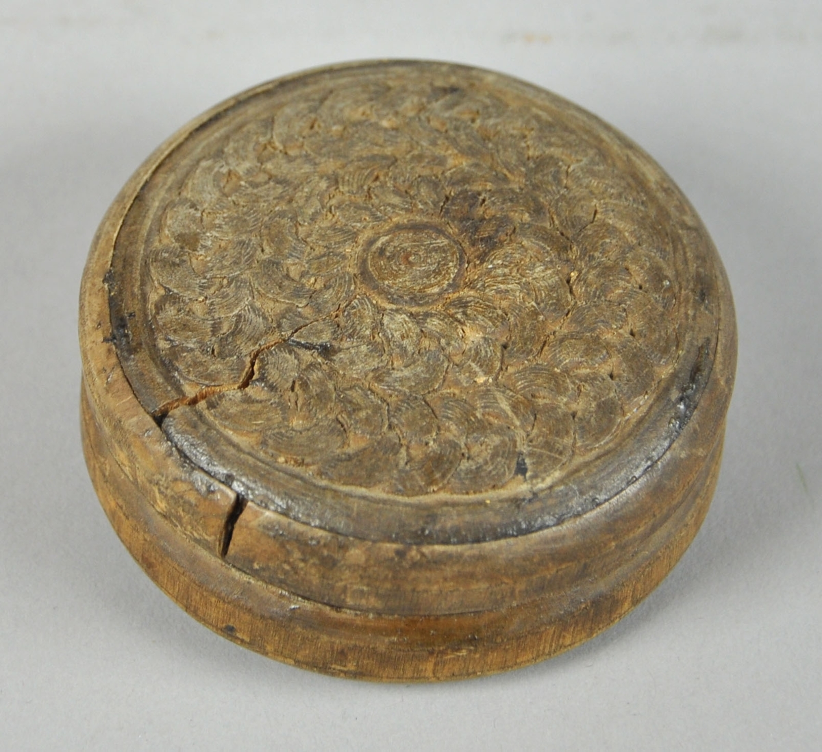 Rund eske av tre, med avtagbart lokk. Skjært dekor med motiv av sirkulære kjettinger på lokk og bunn. Lokket har en betydelig sprekk, som også har ført til misdannelse på lokket.