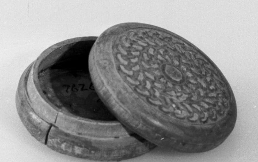 Rund eske av tre, med avtagbart lokk. Skjært dekor med motiv av sirkulære kjettinger på lokk og bunn. Lokket har en betydelig sprekk, som også har ført til misdannelse på lokket.