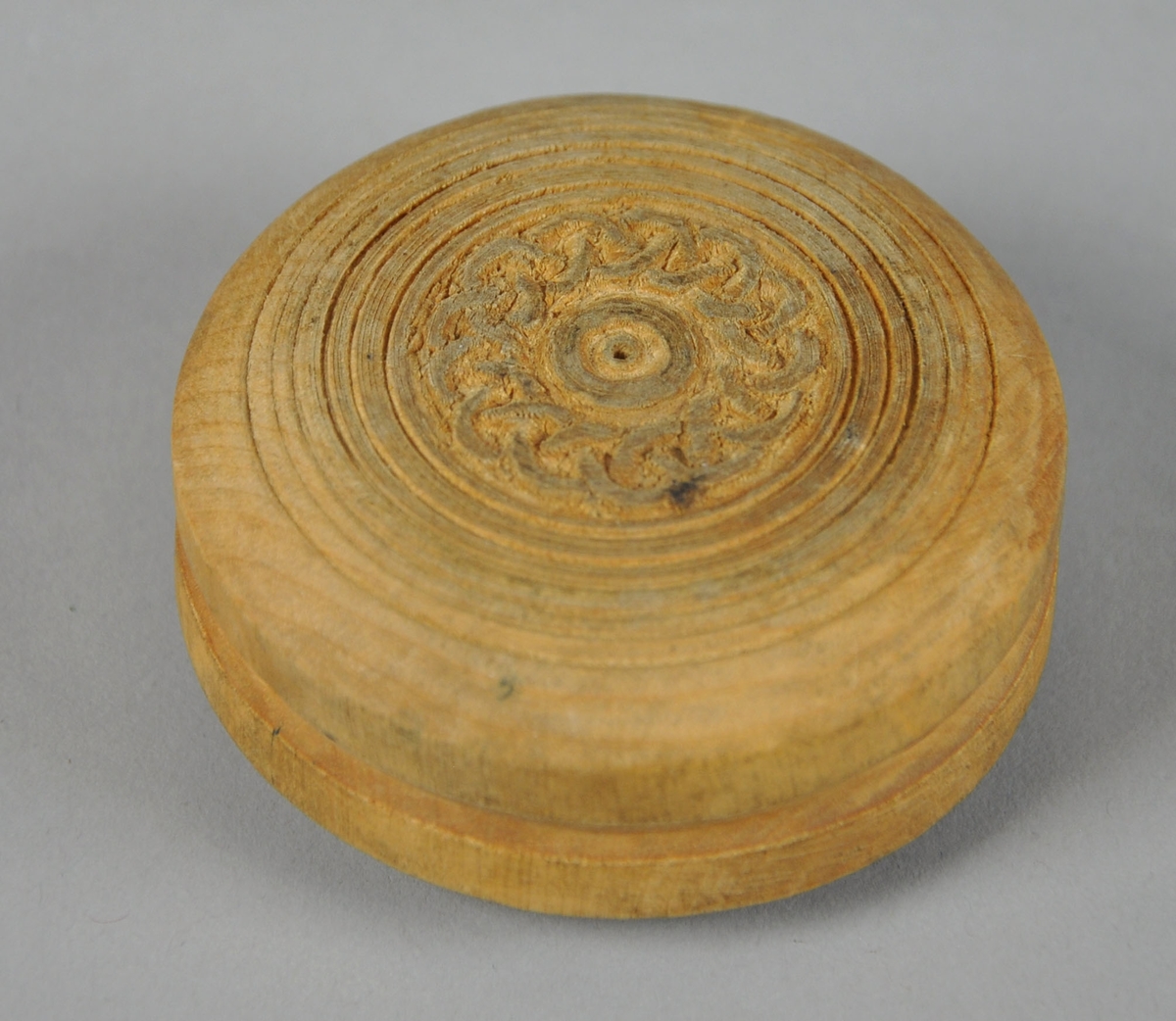 Rund eske av tre, med avtagbart lokk. Esken har innrisset dekor med sirkel- og kjettingmotiv, bunnen har konsentriske sirkler.