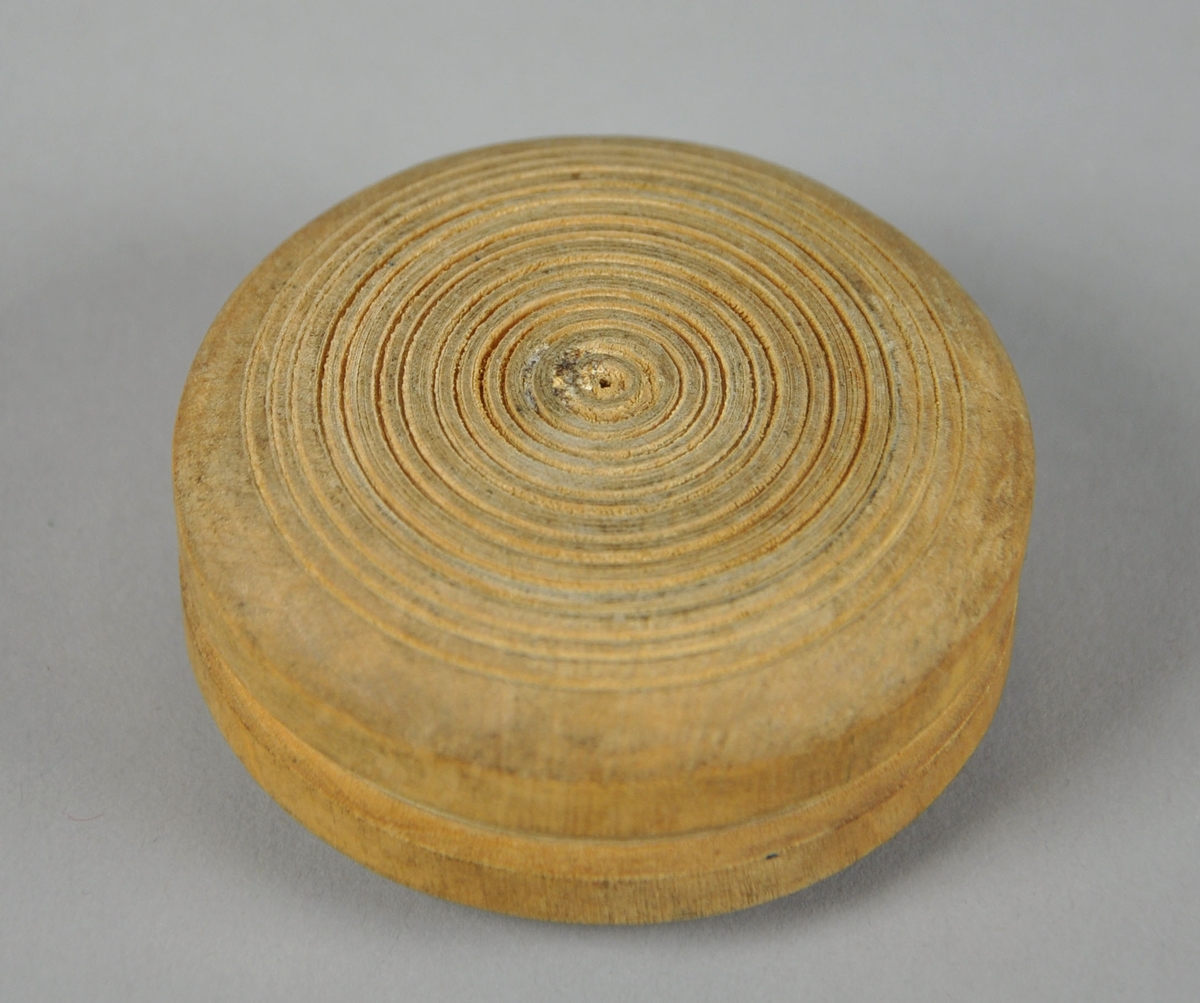Rund eske av tre, med avtagbart lokk. Esken har innrisset dekor med sirkel- og kjettingmotiv, bunnen har konsentriske sirkler.