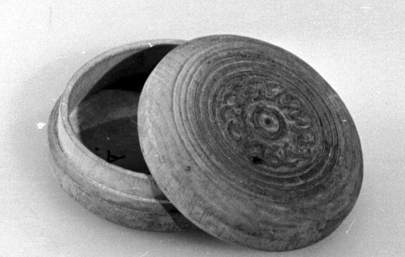 Rund eske av tre, med avtagbart lokk. Esken har innrisset dekor med sirkel- og kjettingmotiv, bunnen har konsentriske sirkler.