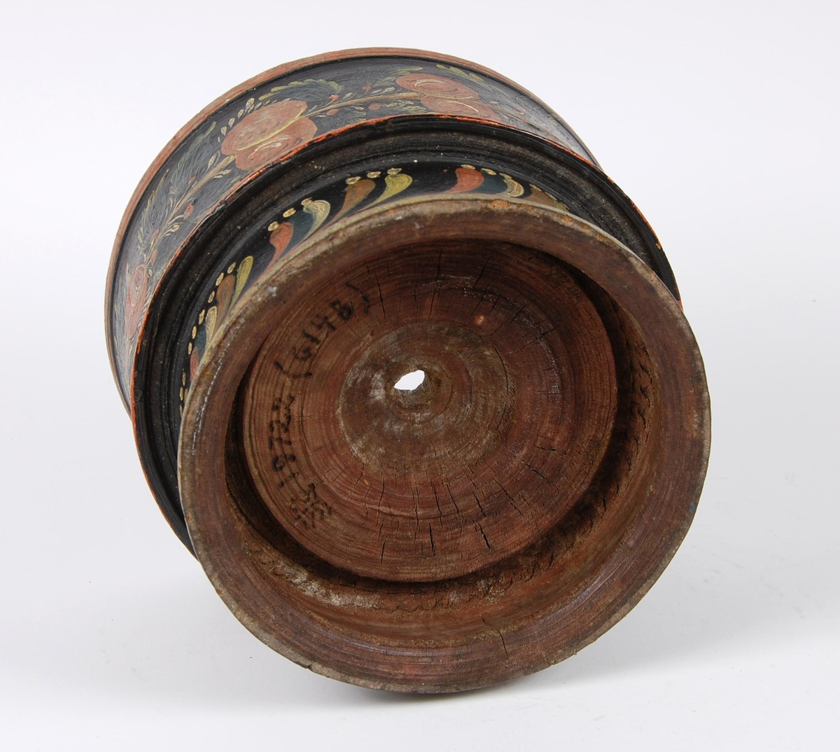 Smørkopp av dreid tre. Koppen har rosemalt dekor med blomstermotiver i ulike farger, røde kanter oppe og nede, hull i bunnen. Stetten har rosemalte skrå stiper.