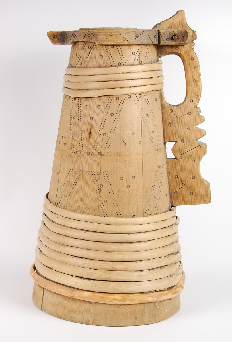 Kanne av trestaver. Lokket har utskåret firebladrose og svidekor i form av rundinger og prikker. Hanken går i ett med en av stavene, har dype hakkformete utskjæringer og noe svidekor i form av rundinger og prikker. Korpus har fire gjorder oppe og ni nede (opprinnelig har det også vært to gjorder midt på. Videre har korpus mye svidekor i form av rundinger og prikker. Underside har innsvidd innskrift