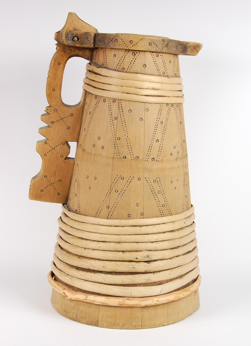 Kanne av trestaver. Lokket har utskåret firebladrose og svidekor i form av rundinger og prikker. Hanken går i ett med en av stavene, har dype hakkformete utskjæringer og noe svidekor i form av rundinger og prikker. Korpus har fire gjorder oppe og ni nede (opprinnelig har det også vært to gjorder midt på. Videre har korpus mye svidekor i form av rundinger og prikker. Underside har innsvidd innskrift