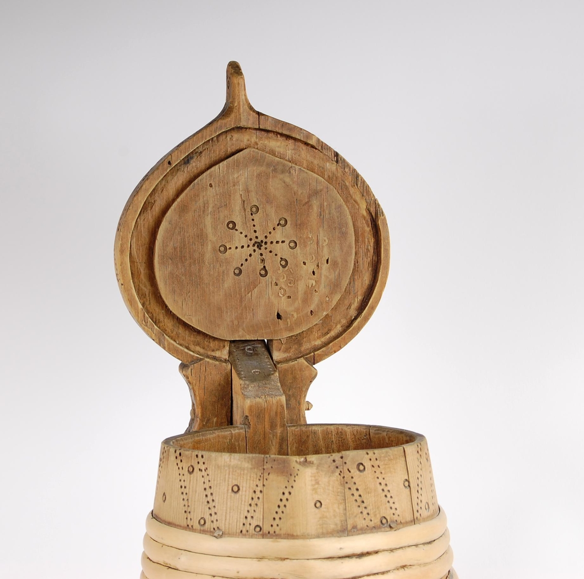 Kanne av trestaver. Lokket har utskåret firebladrose og svidekor i form av rundinger og prikker. Hanken går i ett med en av stavene, har dype hakkformete utskjæringer og noe svidekor i form av rundinger og prikker. Korpus har fire gjorder oppe og ni nede (opprinnelig har det også vært to gjorder midt på. Videre har korpus mye svidekor i form av rundinger og prikker. Underside har innsvidd innskrift