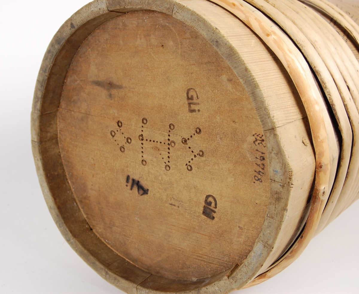 Kanne av trestaver. Lokket har utskåret firebladrose og svidekor i form av rundinger og prikker. Hanken går i ett med en av stavene, har dype hakkformete utskjæringer og noe svidekor i form av rundinger og prikker. Korpus har fire gjorder oppe og ni nede (opprinnelig har det også vært to gjorder midt på. Videre har korpus mye svidekor i form av rundinger og prikker. Underside har innsvidd innskrift