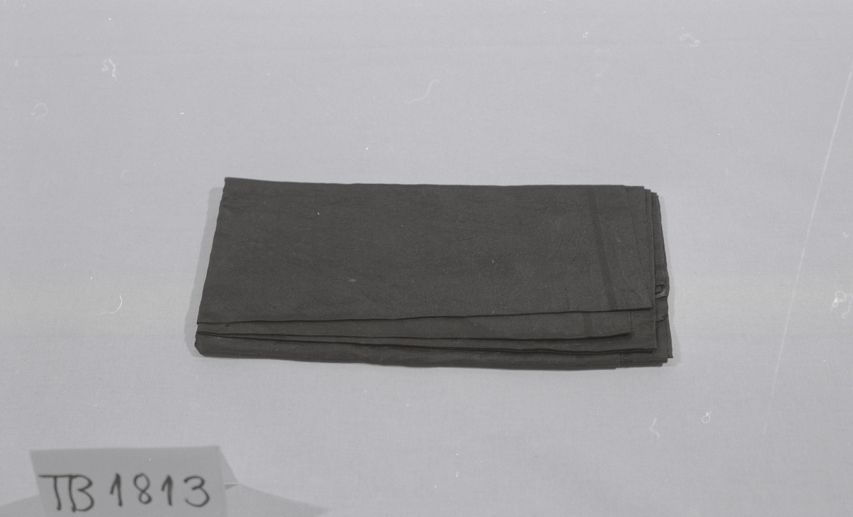 Firkantet, ganske stort, tørkle. Innvevd stripe langs kantene. Full vevbredde. Lagt opp for hånd på to kanter.