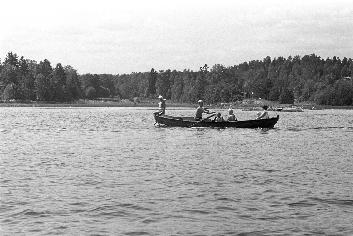 Erik Damman, reklamekonsulent fra Oslo, ferierer i båt med familien i Oslofjorden. De skal ro 10 - 12 mil i løpet av 8 - 10 dager, og går i land på små holmer som fjorden har mange av.  Fra venstre forut Rein (10), Erik Damman, Brede (5), Are (8) og Ranghild Damman sammen med minstemann Jaran (1,5).