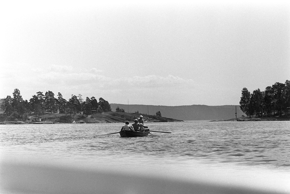 Erik Damman, reklamekonsulent fra Oslo, ferierer i båt med familien i Oslofjorden. De skal ro 10 - 12 mil i løpet av 8 - 10 dager, og går i land på små holmer som fjorden har mange av.  Her er Rein (10), Erik Damman, Brede (5), Are (8), Ranghild Damman og mintemann Jaran (1,5) samlet i båten.