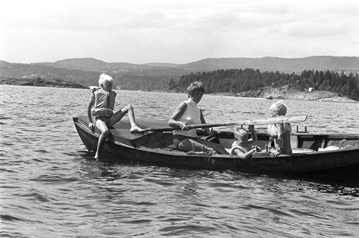 Erik Damman, reklamekonsulent fra Oslo, ferierer i båt med familien i Oslofjorden. De skal ro 10 - 12 mil i løpet av 8 - 10 dager, og går i land på små holmer som fjorden har mange av. Her sitter Ragnhhild Damman ved årene sammen med Are (8), Brede (5) og Rein (10) til venstre forut i båten.