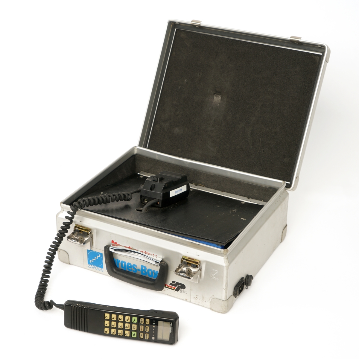 Koffert av metall belagt innvendig med skumgummi, låsbart lokk ,håndtak og  inneholdene et mobiltelefon  håndsett som er  festet til en holder . Håndsettet har et vindu på toppen og under dette er det diverse gummierte funksjonstaster og talltaster. lHolderen er igjen festet til en gjenget skillevegg og under denne finner man en en strømforsyningsenhet og mobiltelefonens hovedenhet. Videre finnes en antenne med kabel og magnetfot til å sette på eks. et biltak. Det medfølger en 240 volts strømkabel samt to 12 volts kabler med kontakter som er tilpasset et 12 volts uttak i en bil.Kofferten har et 240 volts og 12 volts uttak på siden.