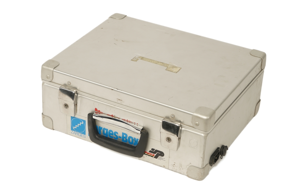 Koffert av metall belagt innvendig med skumgummi, låsbart lokk ,håndtak og  inneholdene et mobiltelefon  håndsett som er  festet til en holder . Håndsettet har et vindu på toppen og under dette er det diverse gummierte funksjonstaster og talltaster. lHolderen er igjen festet til en gjenget skillevegg og under denne finner man en en strømforsyningsenhet og mobiltelefonens hovedenhet. Videre finnes en antenne med kabel og magnetfot til å sette på eks. et biltak. Det medfølger en 240 volts strømkabel samt to 12 volts kabler med kontakter som er tilpasset et 12 volts uttak i en bil.Kofferten har et 240 volts og 12 volts uttak på siden.