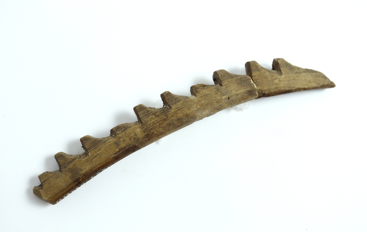 Sågtandad, täljd harpunspets med elva hullingar och snedskuren spets. Avbruten i två delar efter andra hullingen. Plan undersida. Harpunen har genom torkning fått en något böjd form.