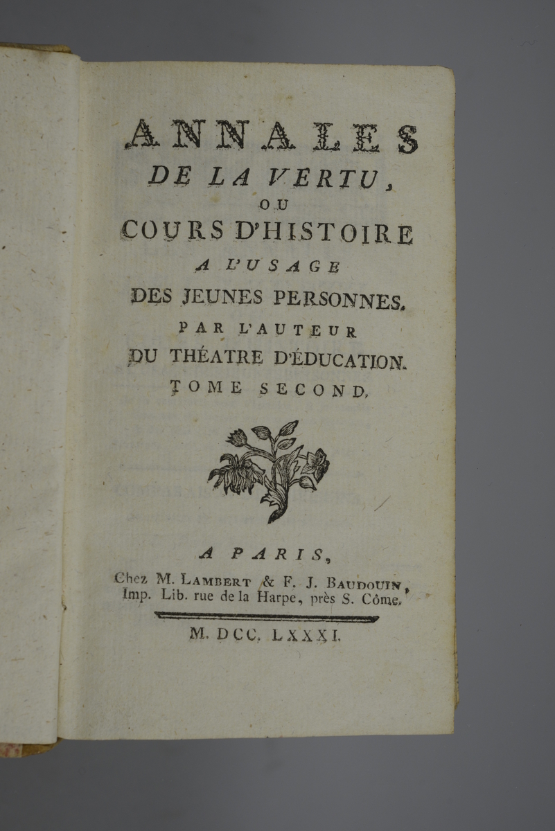 Bok, halvfranskt band " Annales de la vertu ou cours d`histoire a l`usage des jeunes personnes." del II, tryckt i Paris 1781.
Band med rygg av ljust skinn i fyra upphöjda bind, titelfält med blindpressad titel och mörkt fält med volymens nummer. Rester av påklistrad etikett. Pärmen med dekorpapper i rött och vitt. Stänkt snitt.