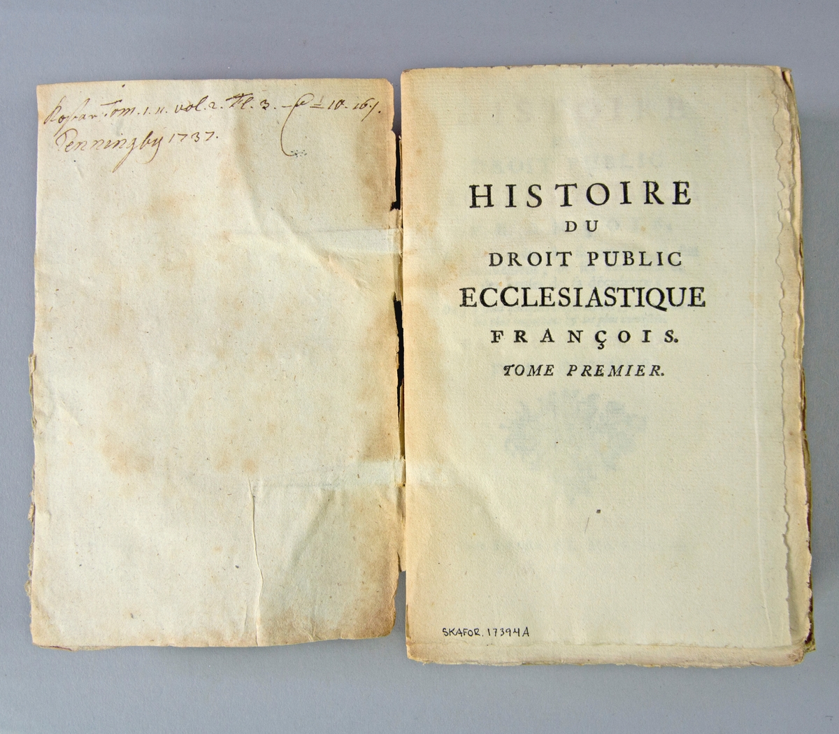 Bok, pappband, "Histoire du droit public ecclesiastique francois", del 1, tryckt 1737 i London. Pärmar av marmorerat papper, blekt rygg med påklistrade etiketter med titel (oläslig)  och samlingsnummer. Oskuret snitt, ouppskuren. Anteckning om inköp på pärmens insida.