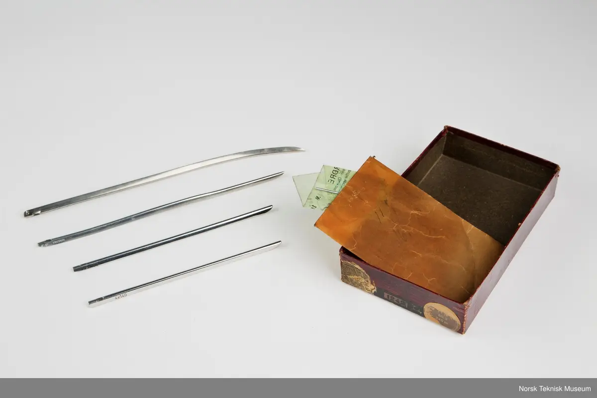 Lokket mangler. Inneholder oljekanne, verktøy, nåler, spoler, rem, symaskinfot, trådsnelle.