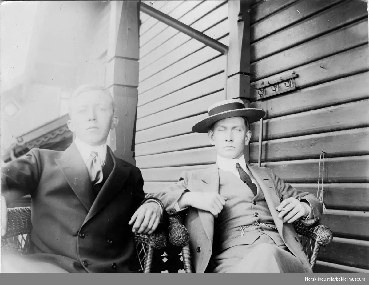 To unge menn i pentøy sittende i kurvstoler på utendørs sitteplass.
