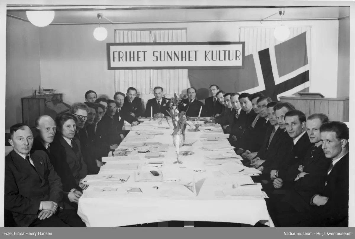 Menn samlet rundt ett bord. Plakat m/tekst; "Frihet Sunnhet Kultur". Idrettsting. Kilde: tekst bak på bildet (247_2)