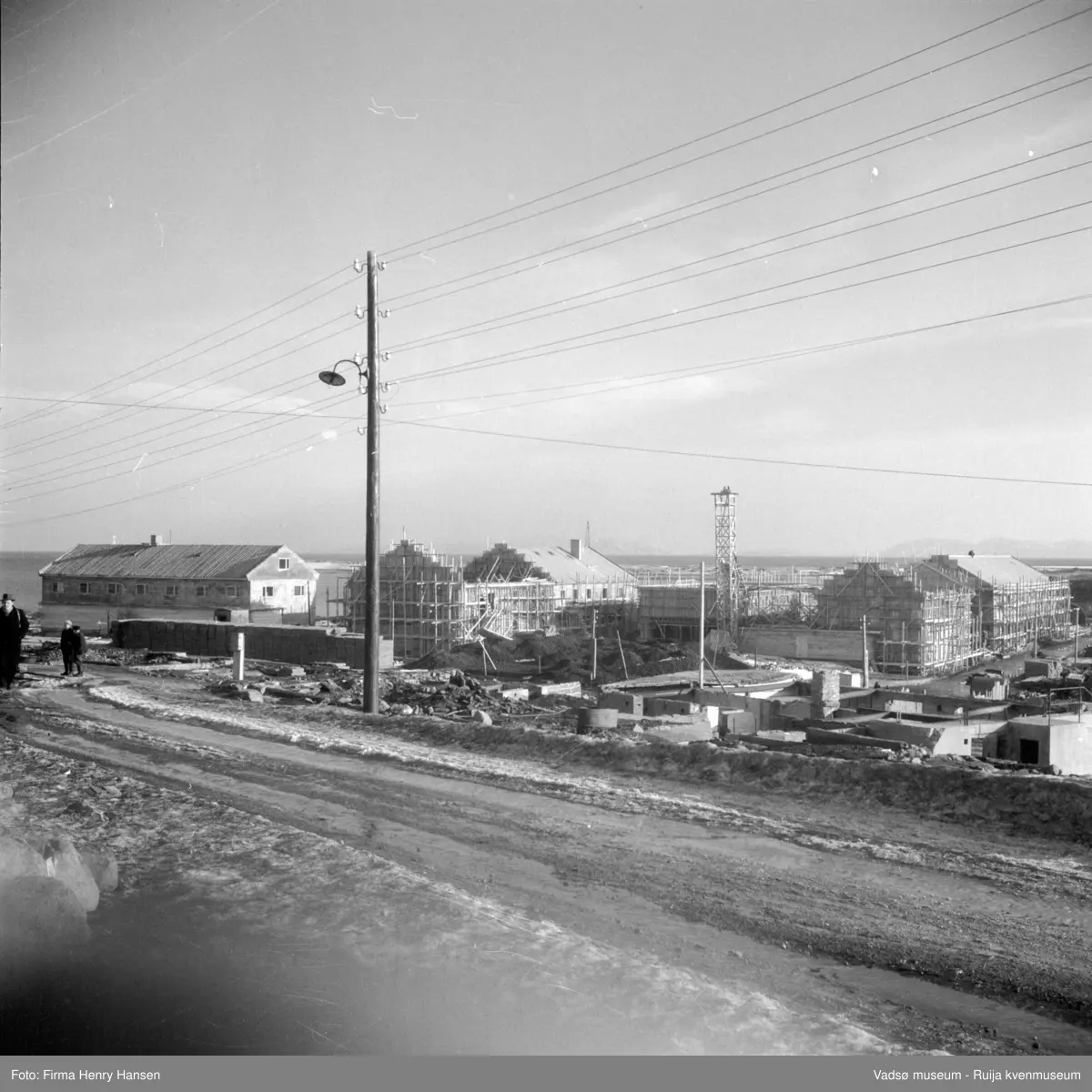Vadsø sentrum. Gjenreisninga av Sentrum i full gang. Forretningsbyggene rundt Torget, øst for Tollbugata ; bla  Rolf Hansen, Henry Hansen og Baker Henriksen under oppføring. Vi ser også forretningsbygget til Leif Bjerck. Bildet er tatt fra Nyborgveien mot sydøst. .