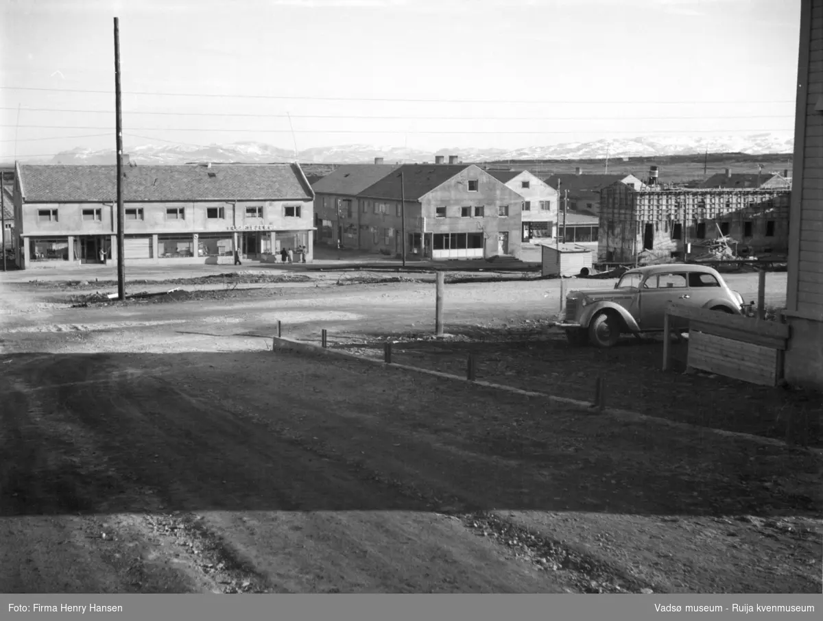 Vadsø mai 1951. Bildet er tatt fra Kirkegata mot syd, med Oscarsgata midt i bildet. Vadsø Rådhus med stillas til høyre i bildet. Vi ser også den lille Drosjebua. Nede i Sentrum forretningsbygget til Leif Bjerck og Baker Henriksen. På torger ser vi deler av Henry Hansens og Rolf Hansens forretningsbygg.ring. I bakkant av bildet skimtes Vadsøya og fjellene på andre siden av fjorden i Sør-Varanger.