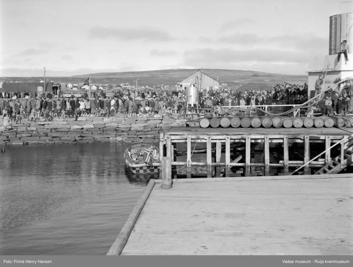 Vadsø. Kongebesøk i Vadsø 1950. Publikum venter på kongen og kronprinsfamilien som skal fraktes fra Kongeskipet Norge inn til land.
Kong Haakon og kronprinsfamilien besøkte Vadsø 25.-26.7.1950 i forbindelse med en større rundreise i Nord-Norge sommeren 1950. Under besøket sto "biltur gjennom byen" og "besøk på sykehuset" på programmet. Kilde: Det kongelige hoff, arkivet