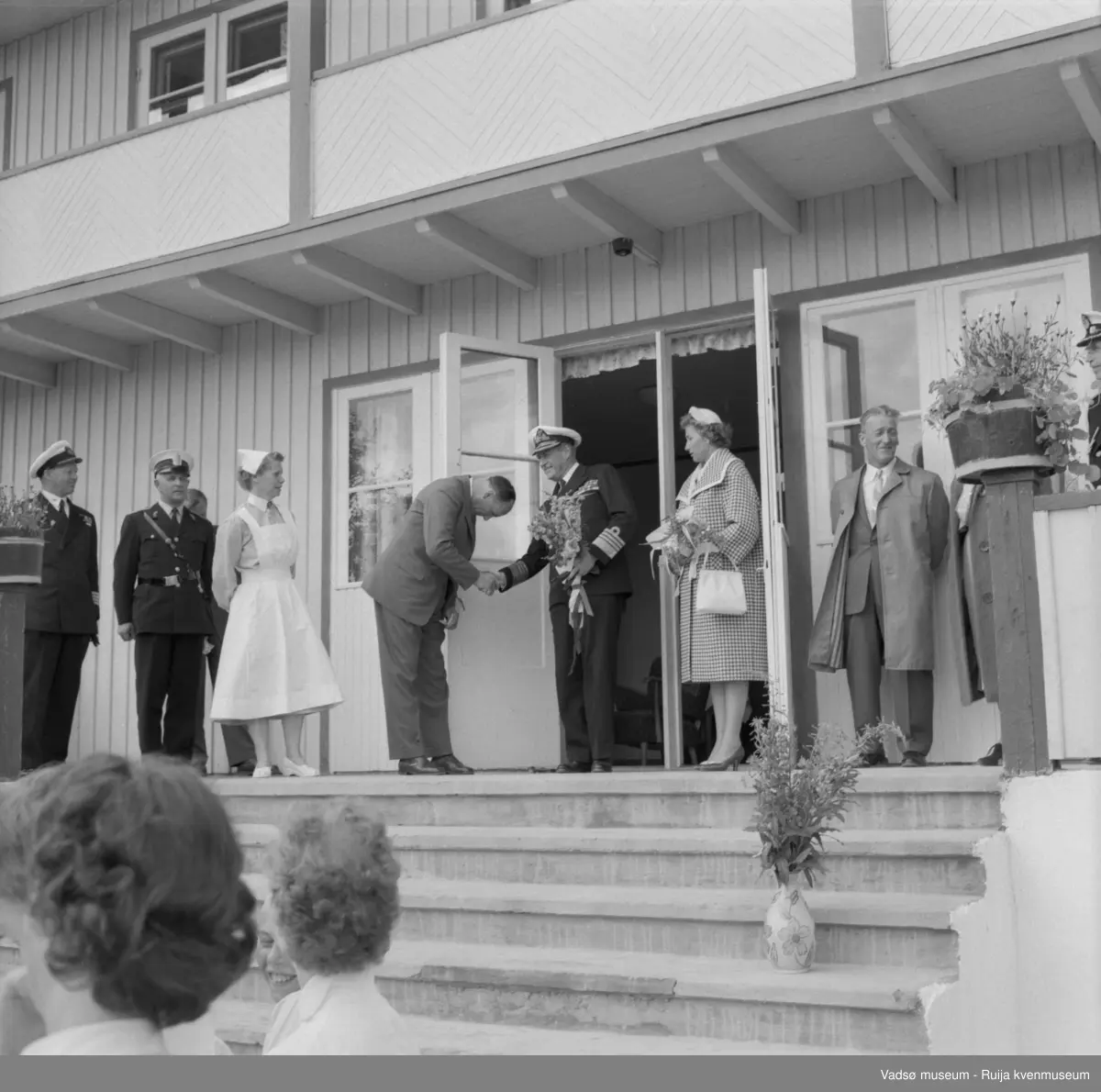 Vestre Jakobselv juli 1959. Kongen på trappa til barnehjemmet Vårsol. Ordfører Henry Karlsen overrekker blomster. Til venstre for kongen, bestyrerinnen søster Gunvor. Til høyre for kongen, prinsesse Astrid og fylkesmann Peder Holt.