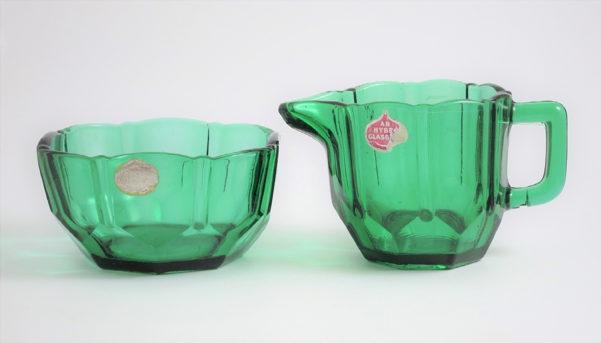 Gräddsnipa med pip och grep.
Runt om facett- och skärslipimitation. 
Etikett: Lila botten med guldfärgad ram och text: AB NYBRO GLASBRUK.