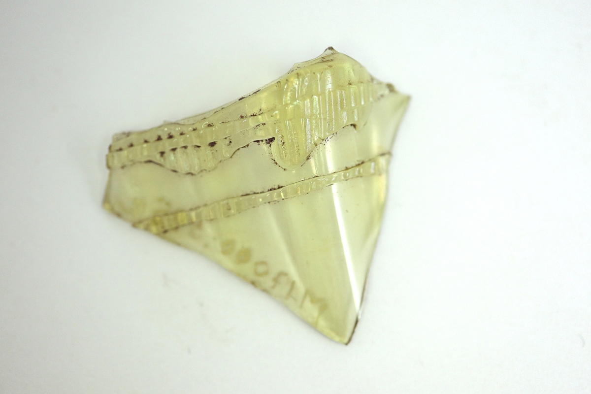 Tre delar av ett brungult, mångkantigt och optikblåst passglas med pålagda strierade trådar.