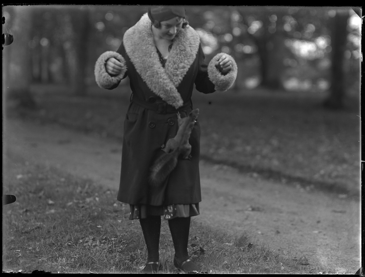 Gulli Svensson fotograferad i en park med en ekorre klättrandes upp för hennes pälskantade kappa.