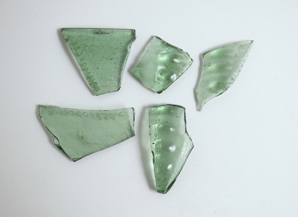 Fem fragment av en kupig bägare (vinglas) av ljusgrön glasmassa. En helt slät mynningsbit (a), tre bukbitar med små bucklor i relief, placerade i vertikala rader (b, c, d) samt en helt slät bukbit (e). M 17000-628 b valdes ut för ICP-analys i maj 2023.