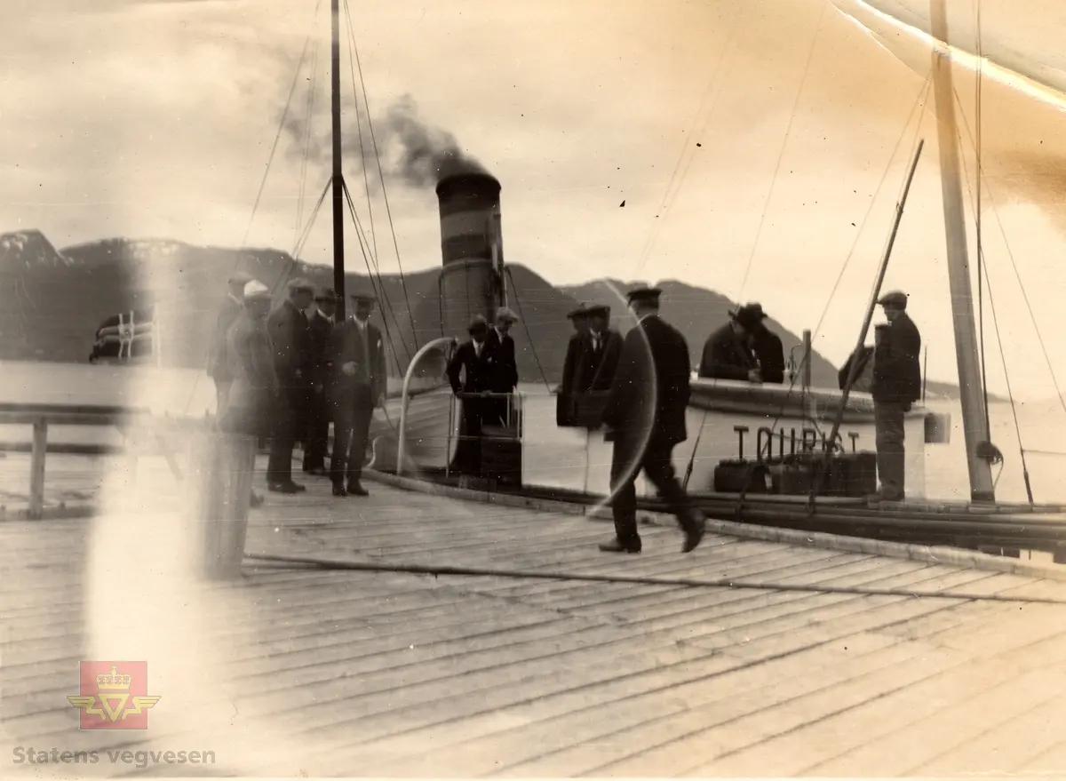 "Tourist ved Sandviken, datert 25.05.1926. I følge merking på baksiden av bildet. Se flere bilder fra befaringen: NVM 00-F-35784, NVM 00-F-35786, NVM 00-F-35788, NVM 00-F-35789 og 35790, som alle er datert 25.05.1926 og registrert hver for seg.

27.09.2018: "Tourist ved Sandviken" viser D/S "Tourist" ved Sandvika kai (Gyl) i Tingvoll kommune med daværende Tingvoll sørland (nå Gjemnes kommune) i bakgrunnen. Opplysninger fra Jon N. Eikrem, Stiftelsen Nordmøre museum, avd. Kristiansund.

27.09.2018: "Godt mulig at dette er en befaring i anledning vegen mellom Gyl (i Tingvoll kommune) og Treekrem (i daværende Straumsnes kommune) – gjennom Gylhamrene – som ble åpnet i 1931 (og utført som nødsarbeid). Sammen med ferjesambandet Kristiansund-Kvisvik (senere Kvalvåg-Kvisvik) som ble åpnet i 1932 (midlertidig utført med dampskip 1931-1932) skapte dette sammenhengende vegforbindelse mellom Kristiansund og Oppdal (dagens RV70). Før 1931 var det f.eks. ikke vegforbindelse mellom Straumsnes kommune og Tingvoll kommune. Ferjesambandet Kvalvåg-Kvisvik ble nedlagt ved åpningen av Krifast (fastlandsforbindelsen til Kristiansund) i 1992. Vesle D/S «Tourist» er nok innleid spesielt for denne befaringen (trafikkerte vanligvis ruta Kristiansund-Batnfjordsøra). Dampskipsruta på Tingvollfjorden (bl.a. med anløp av Øydegard og Sandvika) ble nedlagt i 1957".
Opplysninger fra Jon N. Eikrem, Stiftelsen Nordmøre museum, avd. Kristiansund.