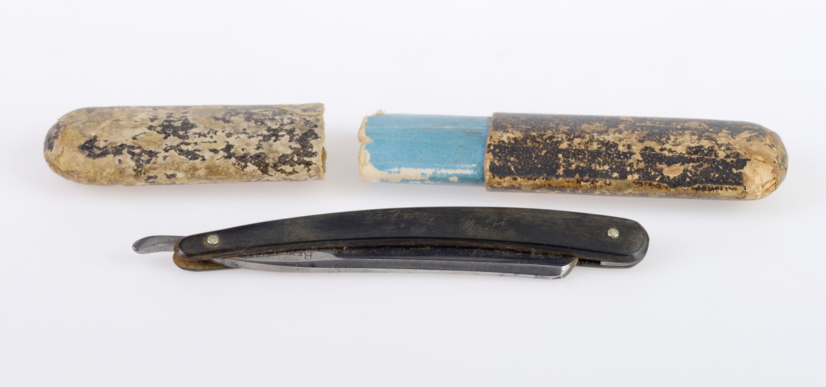 En barberkniv der kniven er laget av stål, mens håndtaket er laget av horn/bein Det er et nedfellbart skarpt blad inni et enkelt håndtak. Håndtaket er svart. Det er primær og sekundær tekst på både knivbladet og på håndtaket, se "Påført tekst/merker". Esken er laget av papp. Utsiden er trukket med svart papir. Esken er ganske slitt. Øverste del av esken kan tas av.