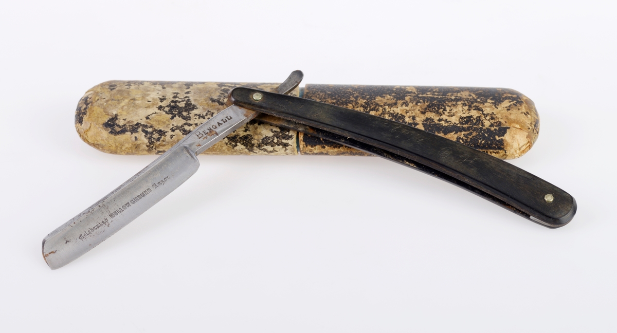 En barberkniv der kniven er laget av stål, mens håndtaket er laget av horn/bein Det er et nedfellbart skarpt blad inni et enkelt håndtak. Håndtaket er svart. Det er primær og sekundær tekst på både knivbladet og på håndtaket, se "Påført tekst/merker". Esken er laget av papp. Utsiden er trukket med svart papir. Esken er ganske slitt. Øverste del av esken kan tas av.