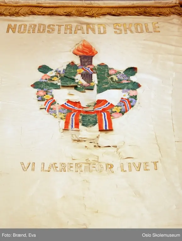 Alle fanene: Stilisert laubærkrans pyntet med blomster og bånd. I midten er det en spirende kvist og en tent fakkel. Øverst på fanen står skolens navn. Nederst på fanen står teksten "Vi lærer for livet" som er skolens visjon. Bakgrunnen er hvit.