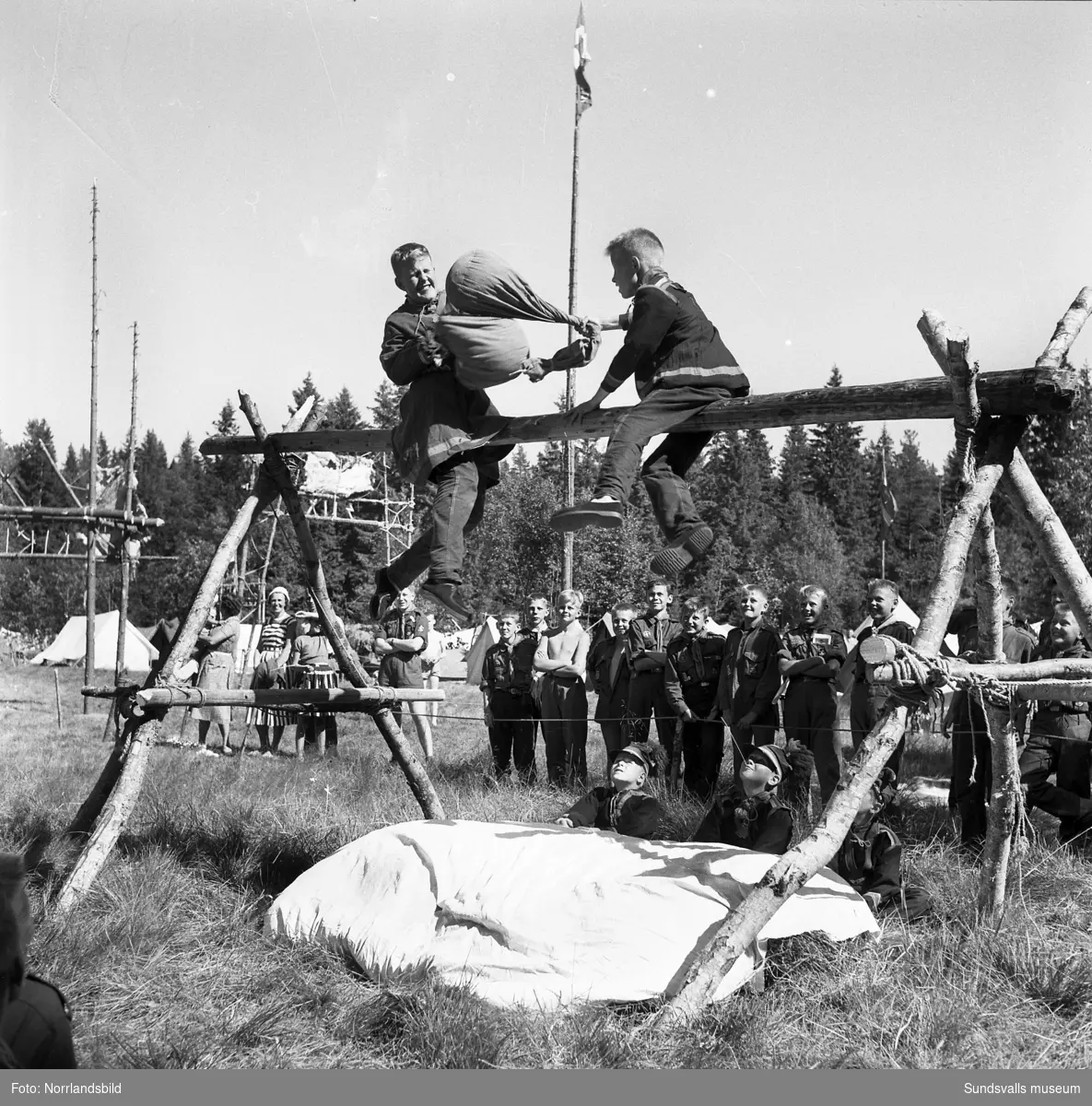 I juli 1959 anordnade Svenska Scoutförbundet sitt stora internationella läger på Rödön utanför Alnö. På första bilden ses lägerledaren Tage Allegård anlända med en grupp pojkscouter för några intensiva veckor på ön. Lägret hade förberetts under ett helt år och dagarna innan hade 70 pojkscouter och ledare hjälpts åt att bygga upp de olika lägerbyarna, som fick namn efter olika fyrar.  SCA hade upplåtit en pråm som låg för ankar i hamnen fylld med de matvaror som krävdes för att mätta de cirka 800 deltagarna.