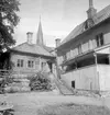 Gårdsinteriör från Storgatan 66 i Linköping. Året är 1953 och arbetet med att flytta utvalda hus i området till friluftsmuseet Gamla Linköping har inletts. Det putsade gårdshuset kommer att rivas men den timrade Skolmästaregården hör till de valda objekten att rädda. Byggnaden uppfördes på platsen i slutet av 1600-talet som tjänstebostad för stadens skolmästare.