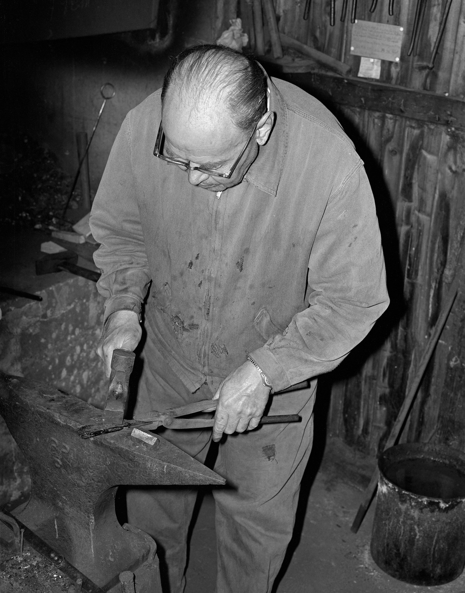 Knivmakeren Even Johannes Blindingsvolden (1908-1985) fra Ringsaker, fotografert ved ambolten i smia, der han bearbeidet varmt knivblademne med en hammer mens han holdt det med ei tang.  Den på dette tidspunktet 65 år gamle håndverkeren var kledd i dongeriklær mens han arbeidet.  Blindingsvolden eide og bodde på småbruket Rudsland på Rudshøgda.  Her hadde han et et 43 kvadratmeter stort hus ved Prestvegen som inneholdt smie- og verkstedrom.

Mer informasjon om knivsmeden Even Blindingsvolden finnes under fanene «Bildehistorikk» og «Opplysninger».