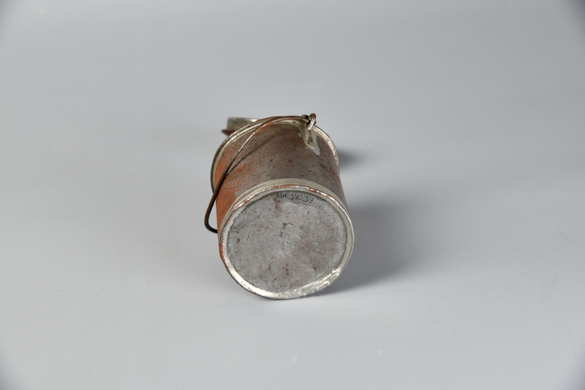 Spann med lokk. Håndtak på lokket og på hver side av korpus. Lokket er løst. Flere slike spann har blitt registrert som melkespann på Digitalt museum. Det er en del rust på oversiden av lokket og den ene siden av spannet.